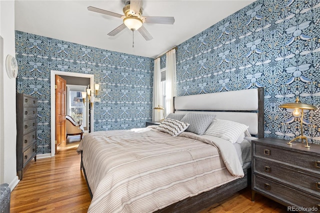 bedroom with wallpapered walls, a ceiling fan, and wood finished floors