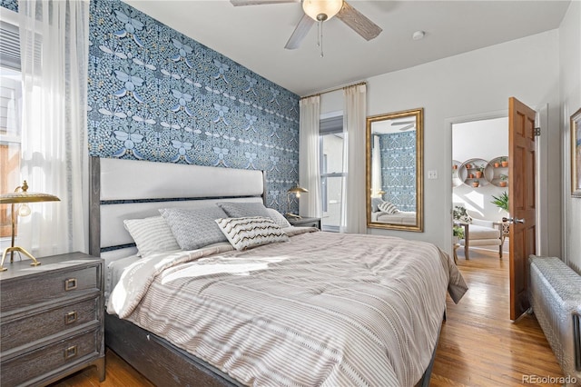 bedroom featuring wallpapered walls, an accent wall, a ceiling fan, and wood finished floors