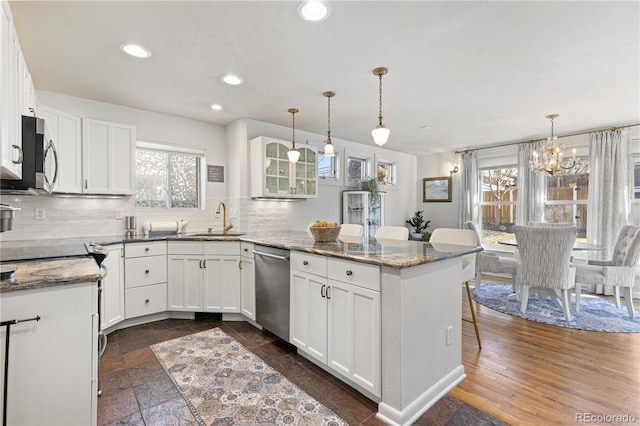 kitchen with appliances with stainless steel finishes, a peninsula, a sink, white cabinetry, and backsplash