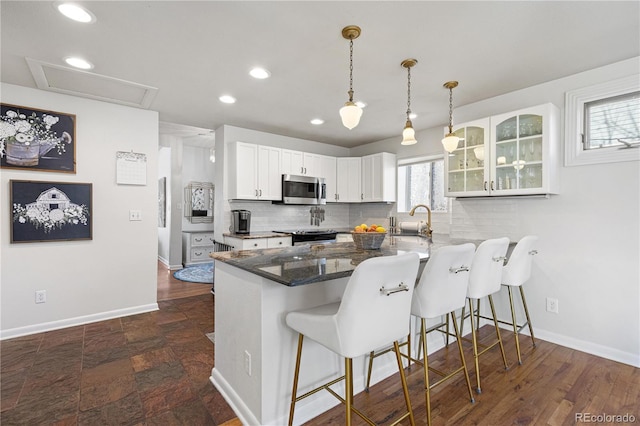 kitchen featuring stainless steel microwave, backsplash, white cabinetry, a peninsula, and a kitchen breakfast bar