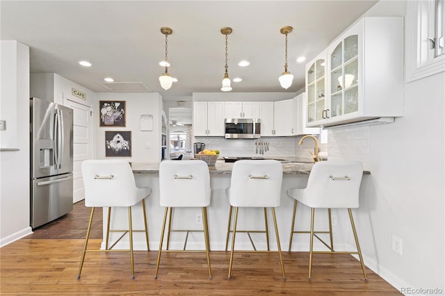 kitchen with stainless steel appliances, a peninsula, wood finished floors, backsplash, and glass insert cabinets