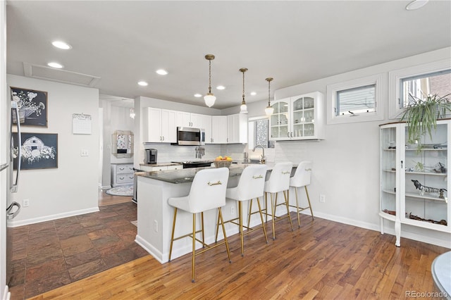 kitchen with a breakfast bar area, tasteful backsplash, stainless steel microwave, a sink, and a peninsula