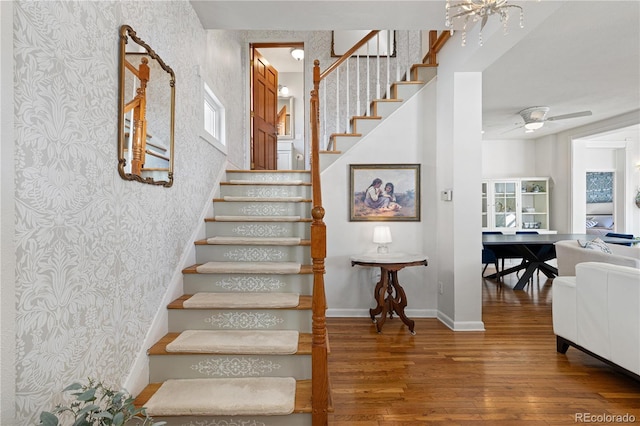 stairway with a ceiling fan, wood finished floors, baseboards, and wallpapered walls