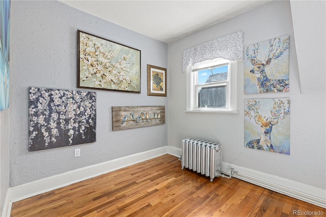 spare room featuring radiator, baseboards, and wood finished floors