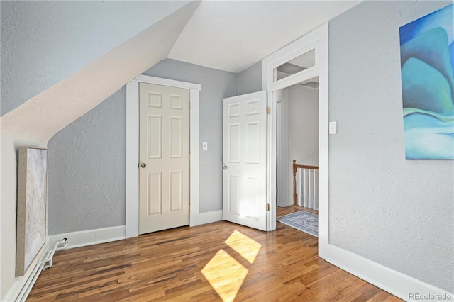 additional living space with baseboards, wood finished floors, and a textured wall