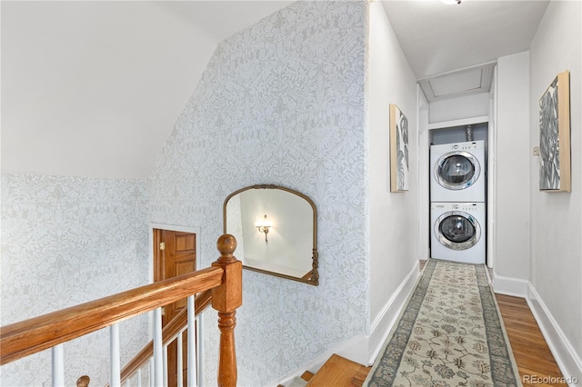 corridor featuring stacked washer / drying machine, wood finished floors, baseboards, and wallpapered walls