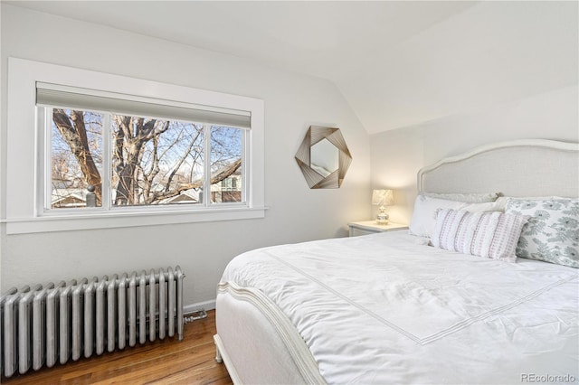 bedroom with lofted ceiling, radiator heating unit, and wood finished floors