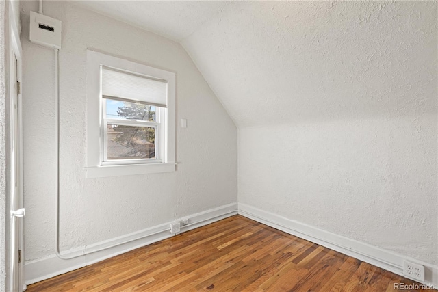 additional living space with baseboards, a textured wall, wood finished floors, vaulted ceiling, and a textured ceiling