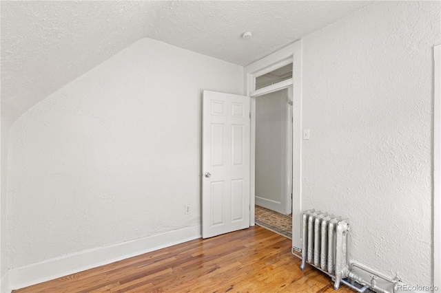 unfurnished bedroom with a textured wall, radiator heating unit, vaulted ceiling, a textured ceiling, and wood finished floors