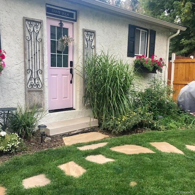 property entrance with fence, a lawn, and stucco siding