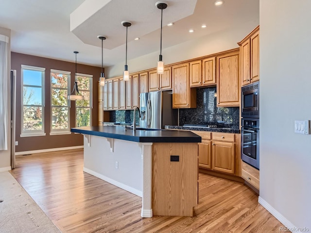 kitchen with backsplash, a center island with sink, sink, light hardwood / wood-style flooring, and stainless steel appliances