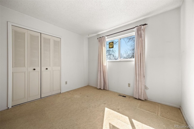 unfurnished bedroom featuring visible vents, carpet, a closet, and a textured ceiling