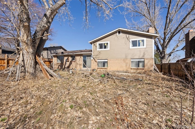 rear view of property with brick siding, a chimney, and fence