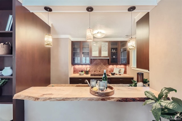 kitchen featuring light countertops, backsplash, decorative light fixtures, and glass insert cabinets