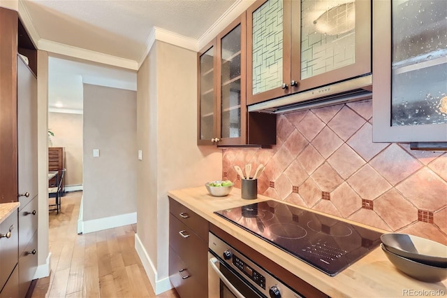 kitchen with crown molding, wall oven, light countertops, black electric stovetop, and under cabinet range hood
