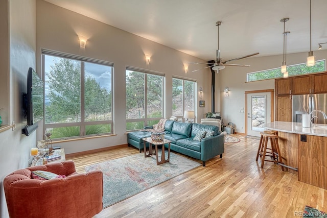 living room featuring ceiling fan, sink, light wood-type flooring, and a wood stove