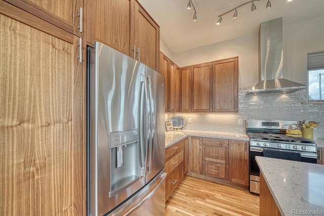 kitchen with stainless steel appliances, light stone counters, decorative backsplash, wall chimney exhaust hood, and light wood-type flooring