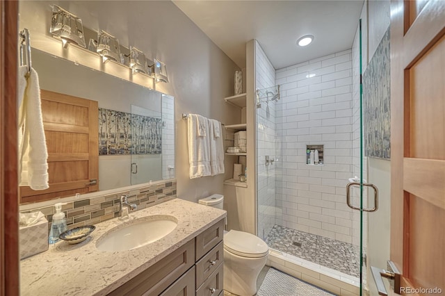 bathroom featuring vanity, toilet, a shower with shower door, and decorative backsplash