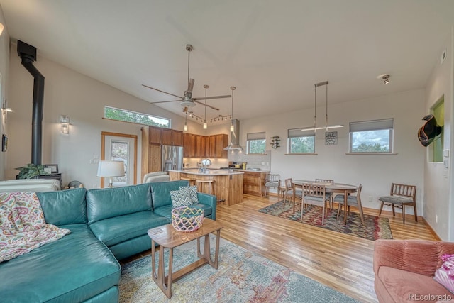 living room with light hardwood / wood-style flooring, ceiling fan, a healthy amount of sunlight, vaulted ceiling, and a wood stove