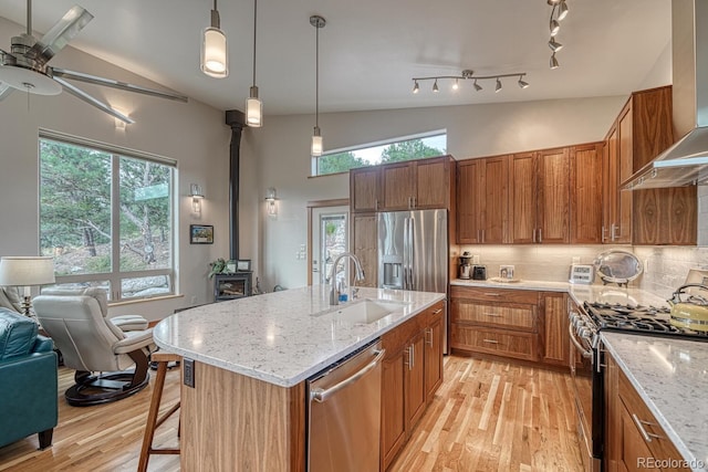 kitchen with sink, a kitchen island with sink, hanging light fixtures, stainless steel appliances, and wall chimney exhaust hood