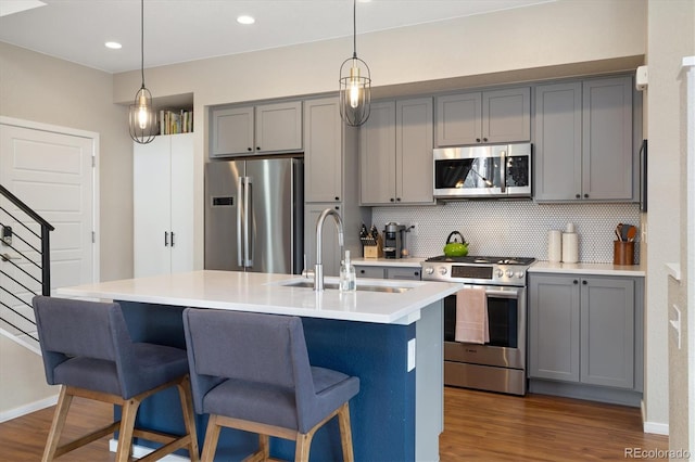 kitchen with appliances with stainless steel finishes, dark wood-type flooring, a sink, and gray cabinetry