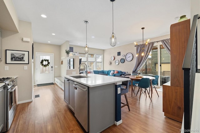 kitchen with light countertops, gray cabinetry, appliances with stainless steel finishes, a sink, and wood finished floors