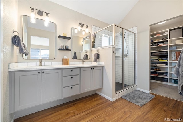 bathroom with wood finished floors, a sink, vaulted ceiling, double vanity, and a stall shower