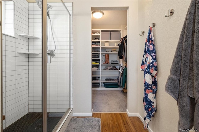 full bathroom featuring a stall shower, a spacious closet, baseboards, and wood finished floors