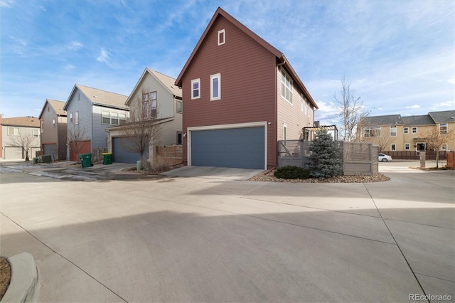 view of side of property with a garage, a residential view, concrete driveway, and fence