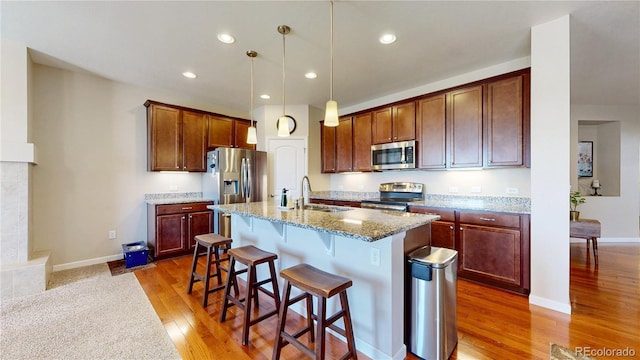 17114 Elati St, Broomfield, CO 80023 - kitchen featuring stainless steel appliances, light wood-style flooring, a breakfast bar area, light stone countertops, and an island with sink