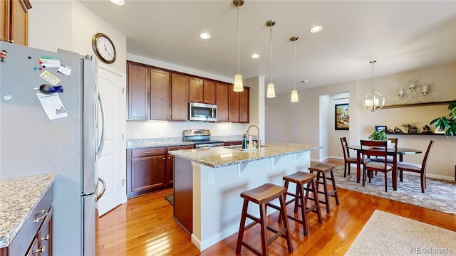 17114 Elati St, Broomfield, CO 80023 - kitchen with appliances with stainless steel finishes, light wood-style floors, a center island with sink, light stone countertops, and recessed lighting