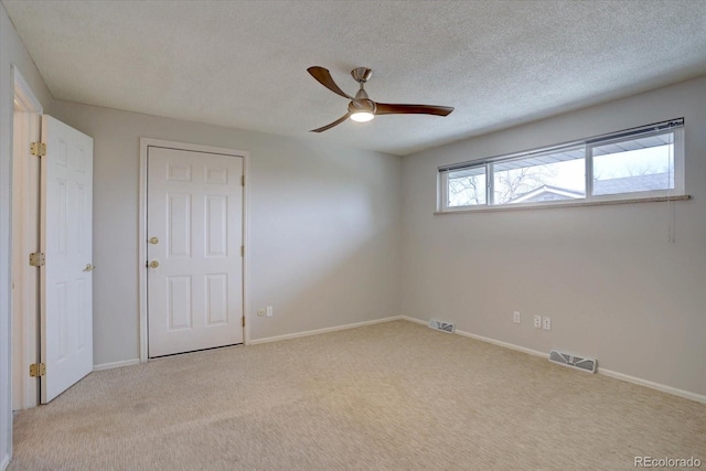carpeted spare room with baseboards, a ceiling fan, a textured ceiling, and visible vents
