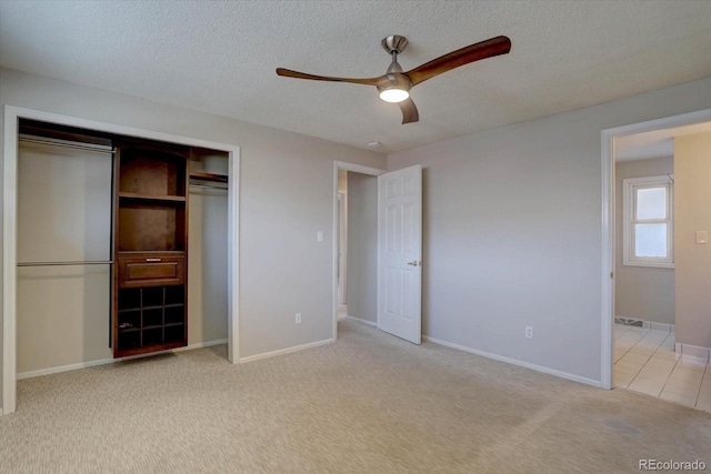 unfurnished bedroom with a closet, baseboards, light colored carpet, a textured ceiling, and a ceiling fan