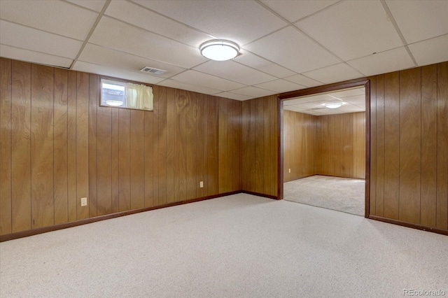 basement featuring carpet flooring, a drop ceiling, and wood walls