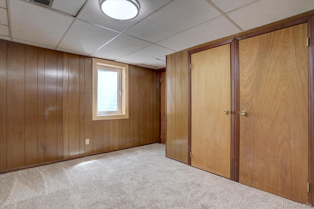 unfurnished bedroom with wood walls, carpet, multiple closets, and a paneled ceiling