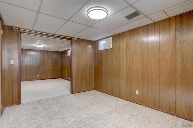 below grade area featuring carpet floors, visible vents, wood walls, and a paneled ceiling