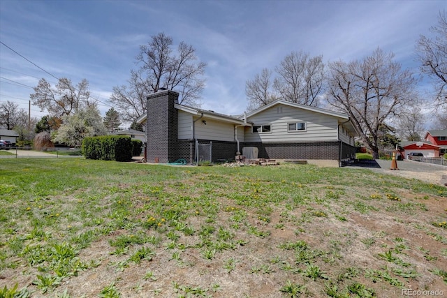 view of property exterior featuring fence, a chimney, a yard, and brick siding