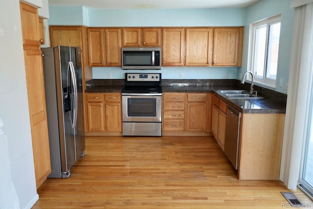 kitchen with appliances with stainless steel finishes, dark countertops, a sink, and light wood finished floors