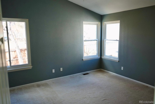 carpeted spare room featuring vaulted ceiling, plenty of natural light, and baseboards