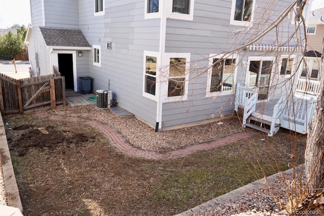 rear view of house with roof with shingles, fence, and central air condition unit