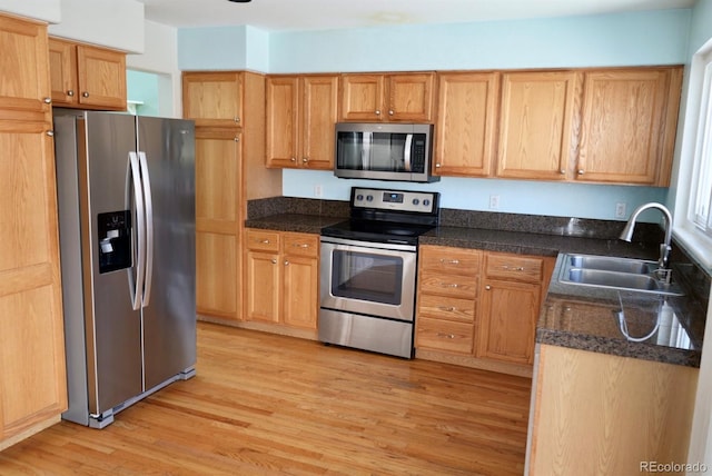 kitchen with light wood-style flooring, appliances with stainless steel finishes, dark stone counters, and a sink