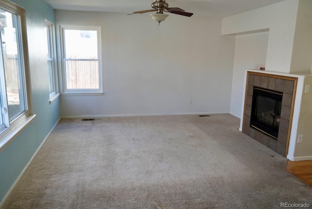 unfurnished living room featuring light colored carpet, visible vents, a tiled fireplace, ceiling fan, and baseboards