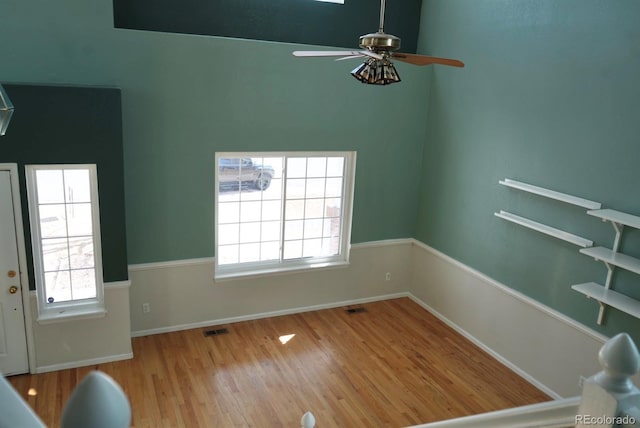 interior space with a ceiling fan, light wood-type flooring, visible vents, and baseboards