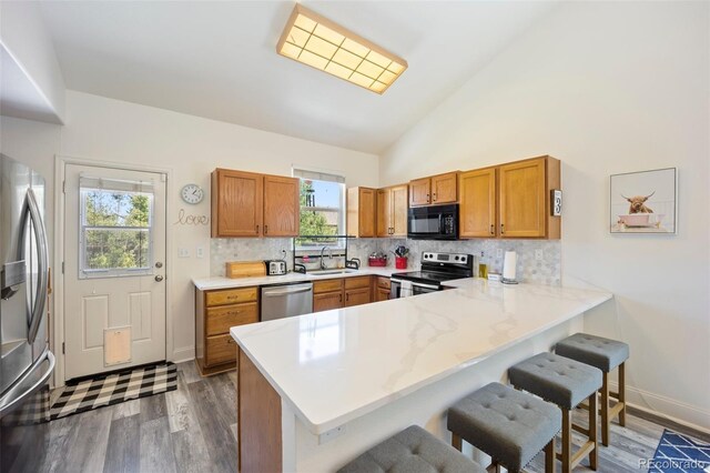 1884 Asoka St, Strasburg, CO 80136 - kitchen featuring stainless steel appliances, a peninsula, wood finished floors, brown cabinetry, and a breakfast bar