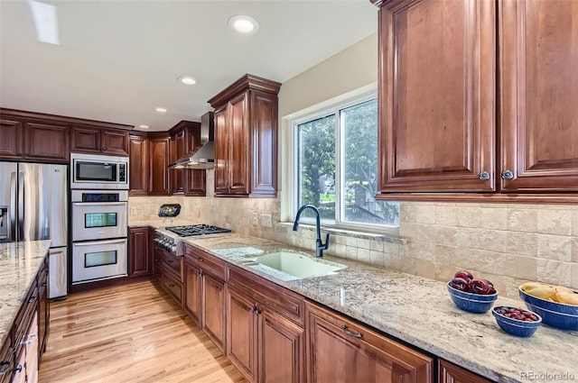 7855 Arundel Ln, Lone Tree, CO 80124 - kitchen featuring appliances with stainless steel finishes, wall chimney exhaust hood, light stone countertops, light wood-style flooring, and tasteful backsplash
