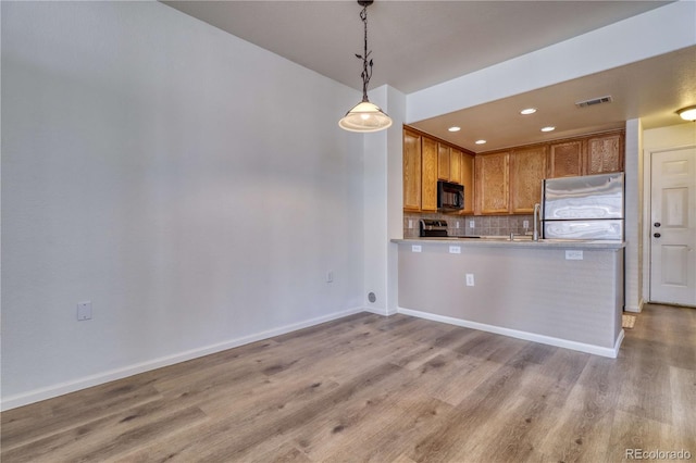 kitchen featuring stove, backsplash, stainless steel fridge, decorative light fixtures, and kitchen peninsula