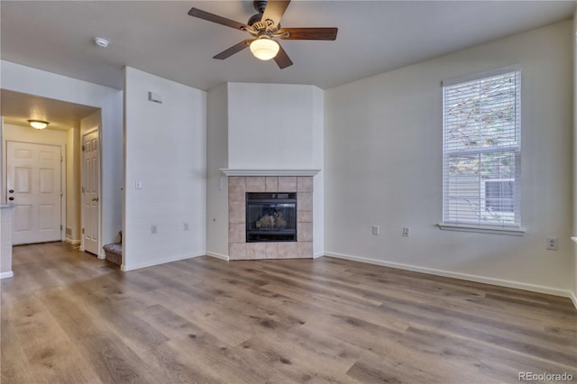 unfurnished living room with a tiled fireplace, ceiling fan, and light wood-type flooring