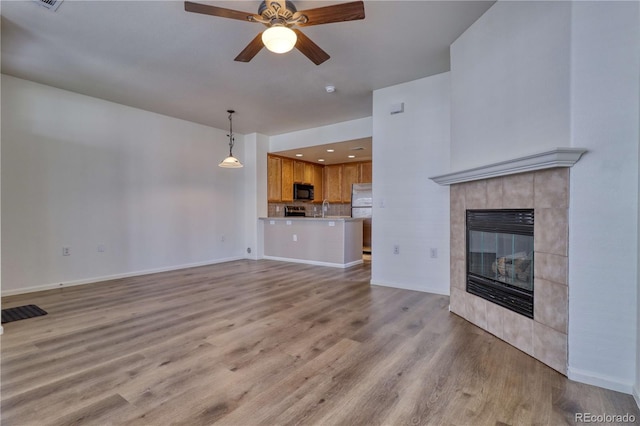 unfurnished living room featuring sink, a fireplace, ceiling fan, and light wood-type flooring