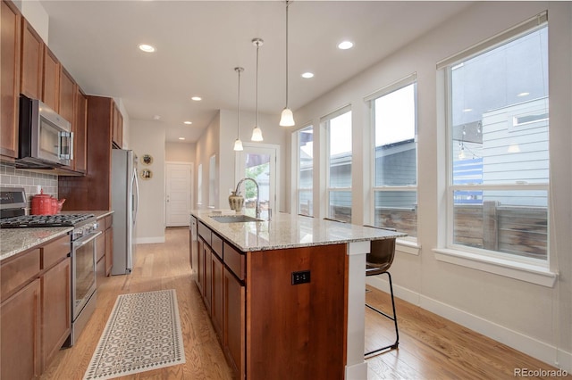 kitchen featuring a center island with sink, appliances with stainless steel finishes, light hardwood / wood-style flooring, pendant lighting, and decorative backsplash