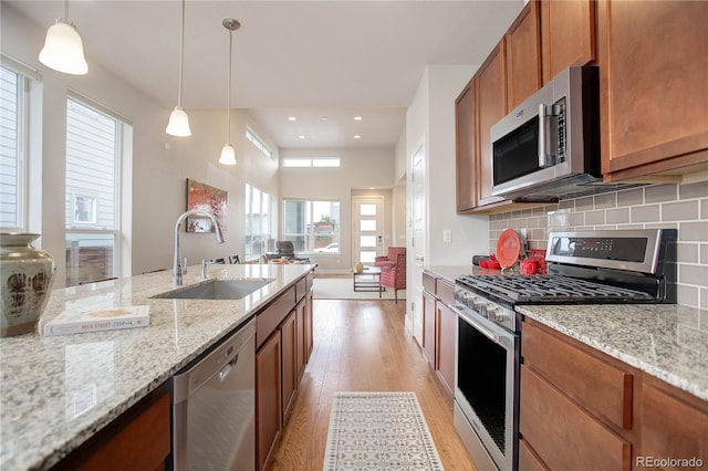 kitchen with stainless steel appliances, light hardwood / wood-style floors, sink, light stone counters, and pendant lighting